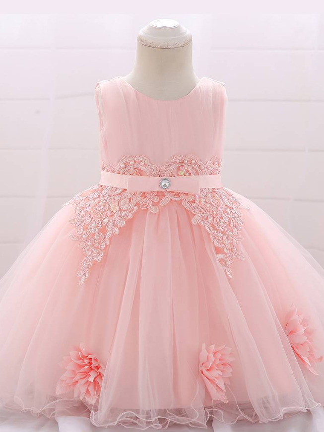 Baby dress has a tulle overlay with flower applique and a satin belt with rhinestone detail-pink