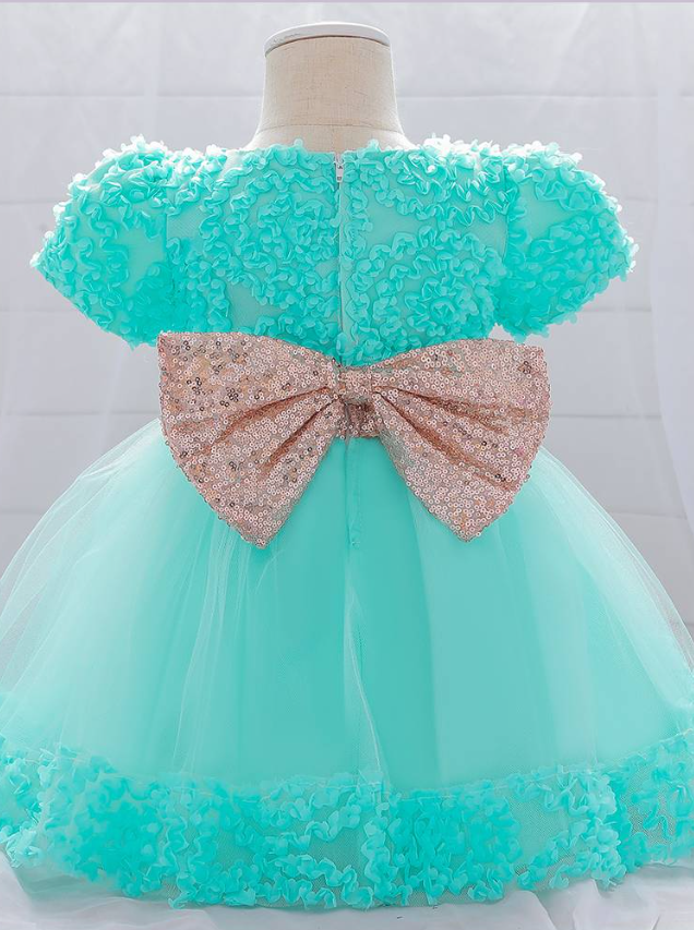 Baby dress has a floral bodice, a tulle skirt with floral hem, and a gold sequin belt with bow at the front and back